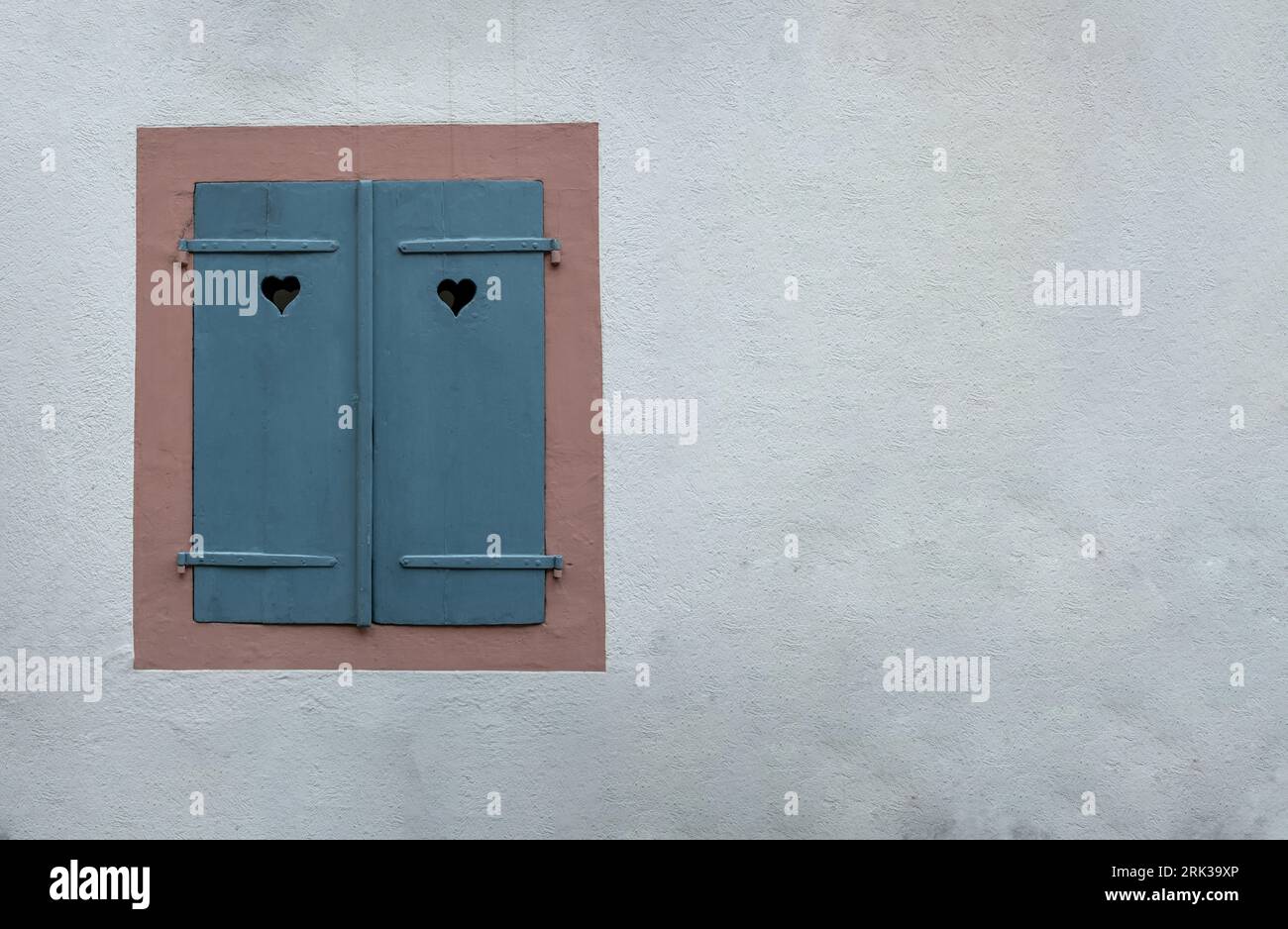 Fenêtre avec volets en bois fermés bleus sur fond de mur en pierre blanche. Obturateur avec trou de coeur, symbole d'amour. Banque D'Images