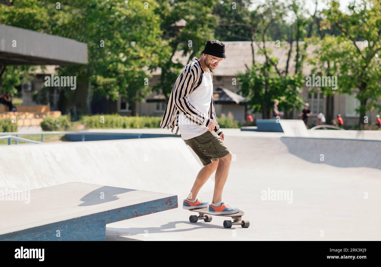 Homme adulte élégant monte un skateboard sur la rampe du skate Park. Pratiquer le skateboard en plein air dans un skate Park par une journée ensoleillée Banque D'Images