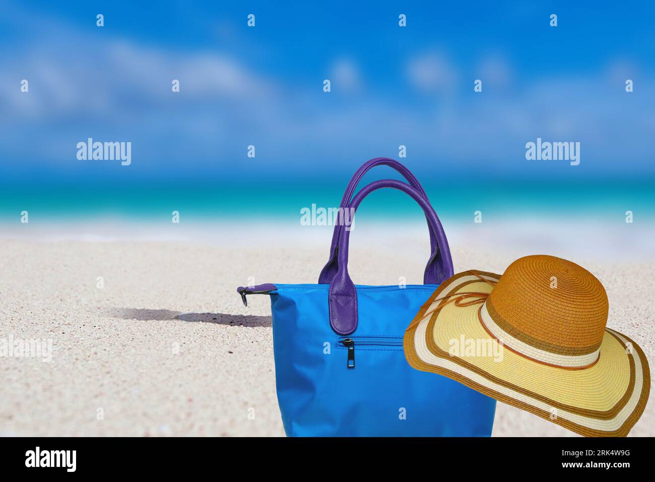 Abstrait flou tropical plage de sable ensoleillé avec fond bleu de l'océan pour les vacances de voyage et sac de plage avec chapeau de paille pour les vacances d'été. Banque D'Images