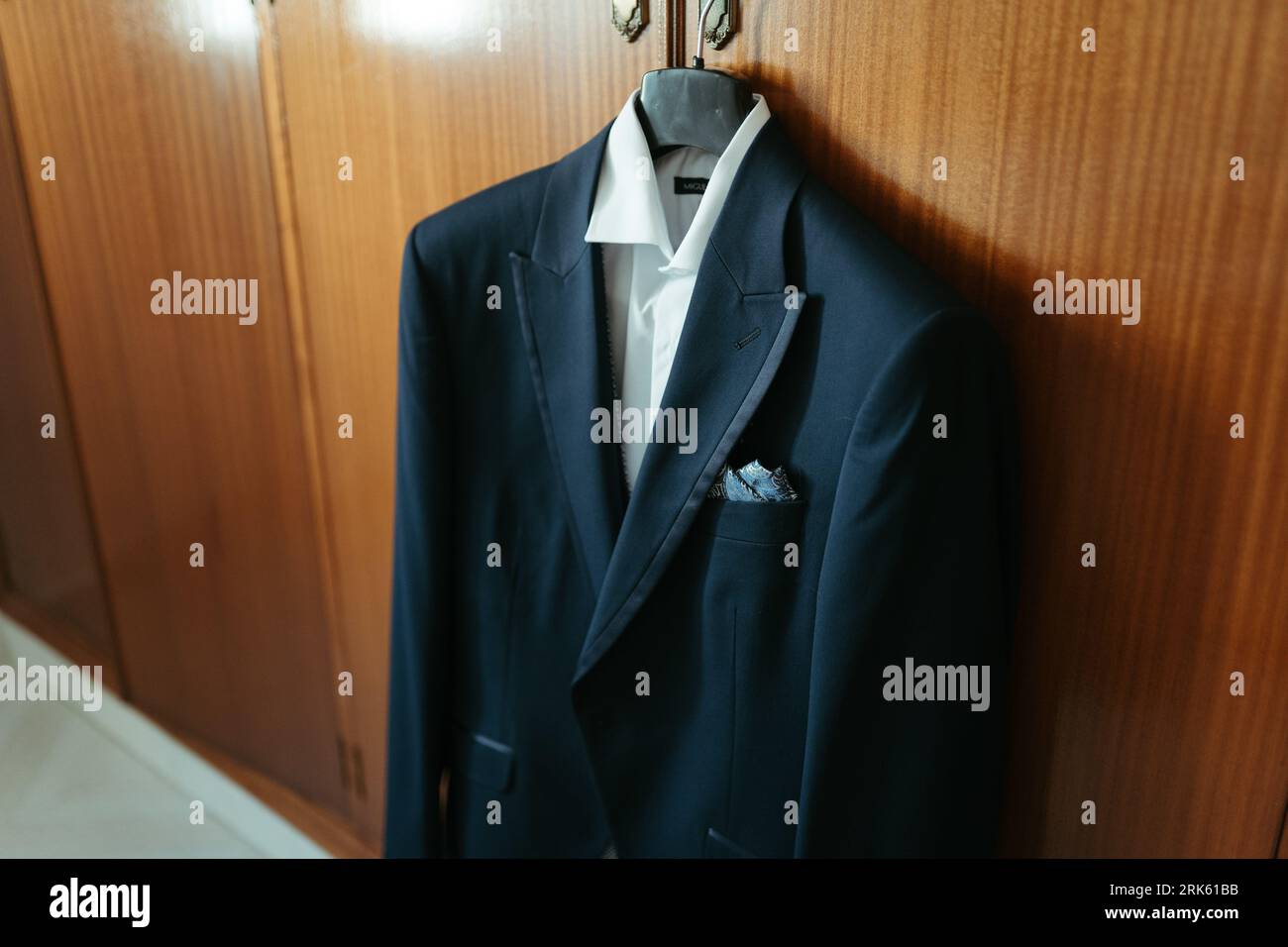 Un costume classique bleu marine est présenté accroché sur un mur de couleur claire, avec une chemise habillée blanche en dessous Banque D'Images