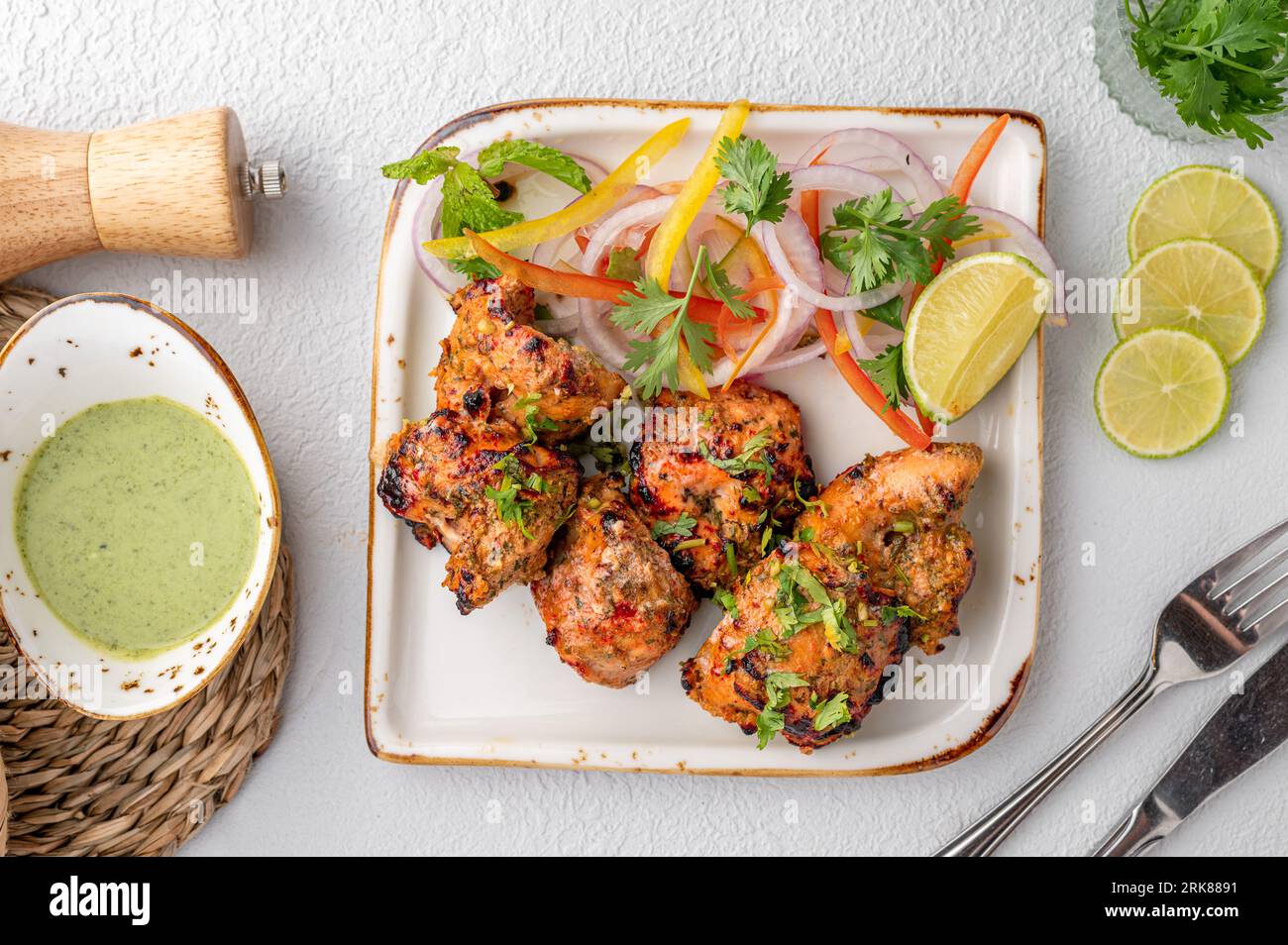 Une assiette de cuisine indienne avec du poulet tandoori, garnie d'oignons parfumés et servie avec un accompagnement de légumes Banque D'Images