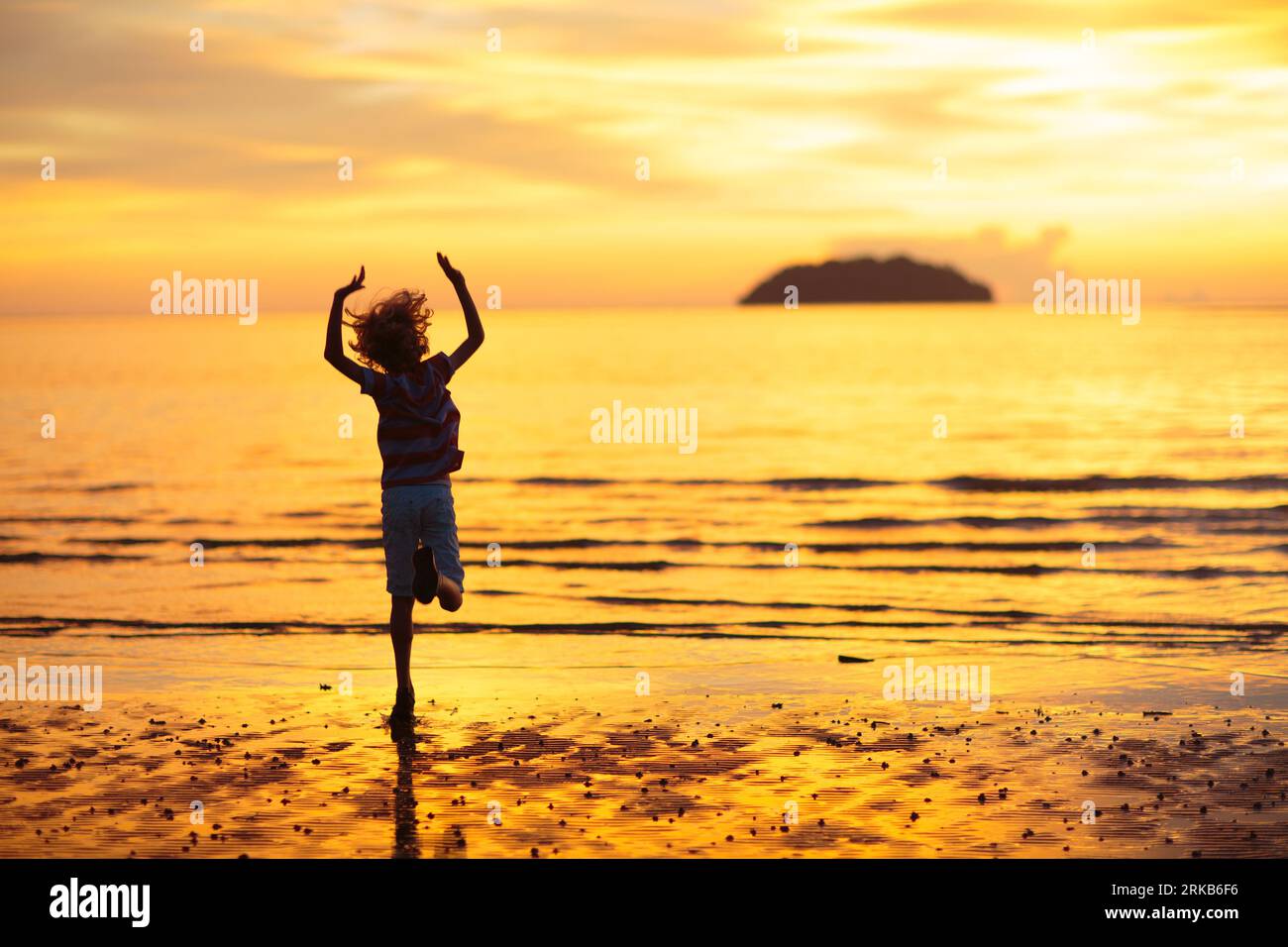 Enfant jouant sur la plage de l'océan. Les enfants sautent dans les vagues au coucher du soleil. Vacances en mer pour la famille. Petit garçon courir sur l'île exotique pendant les vacances d'été. Banque D'Images