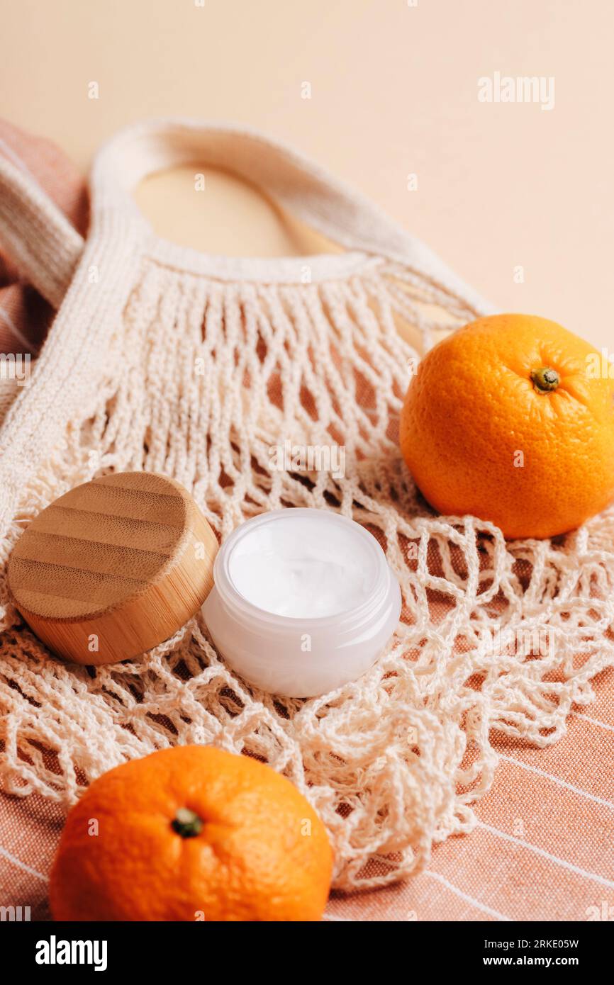 Pot de crème sur le fond de sac en maille de coton et de mandarines. Produit de beauté cosmétique biologique pour spa. Concept zéro déchet. Gros plan. Banque D'Images