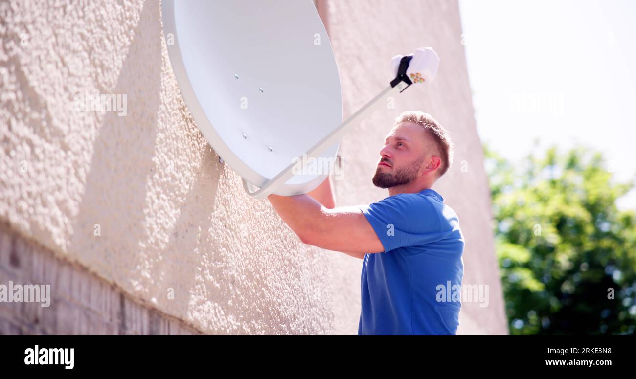 Technicien de jeunes hommes en uniforme de l'installation TV antenne satellite sur le mur Banque D'Images