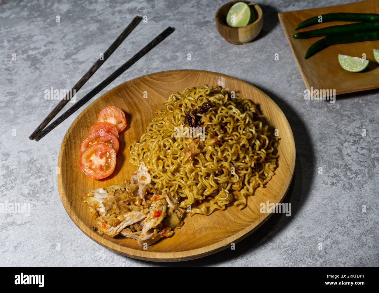 Mie goreng ayam geprek. Nouilles frites servies sur une assiette en bois accompagnées de poulet, tomates fraîches et saupoudrées d'oignons frits Banque D'Images