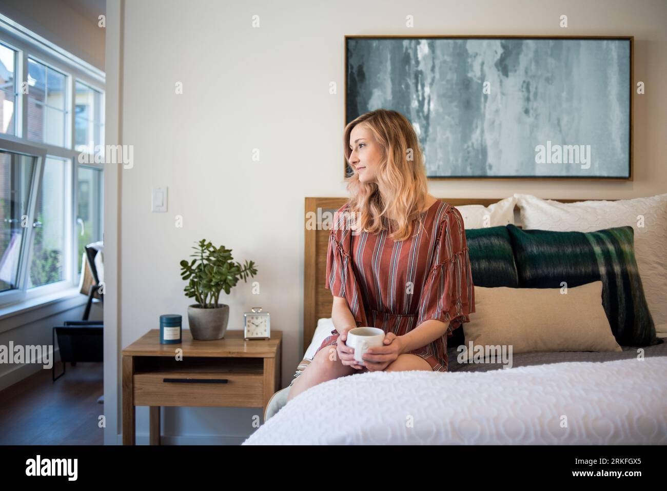 Jeune femme assise sur le lit dans l'appartement avec tasse à café Banque D'Images