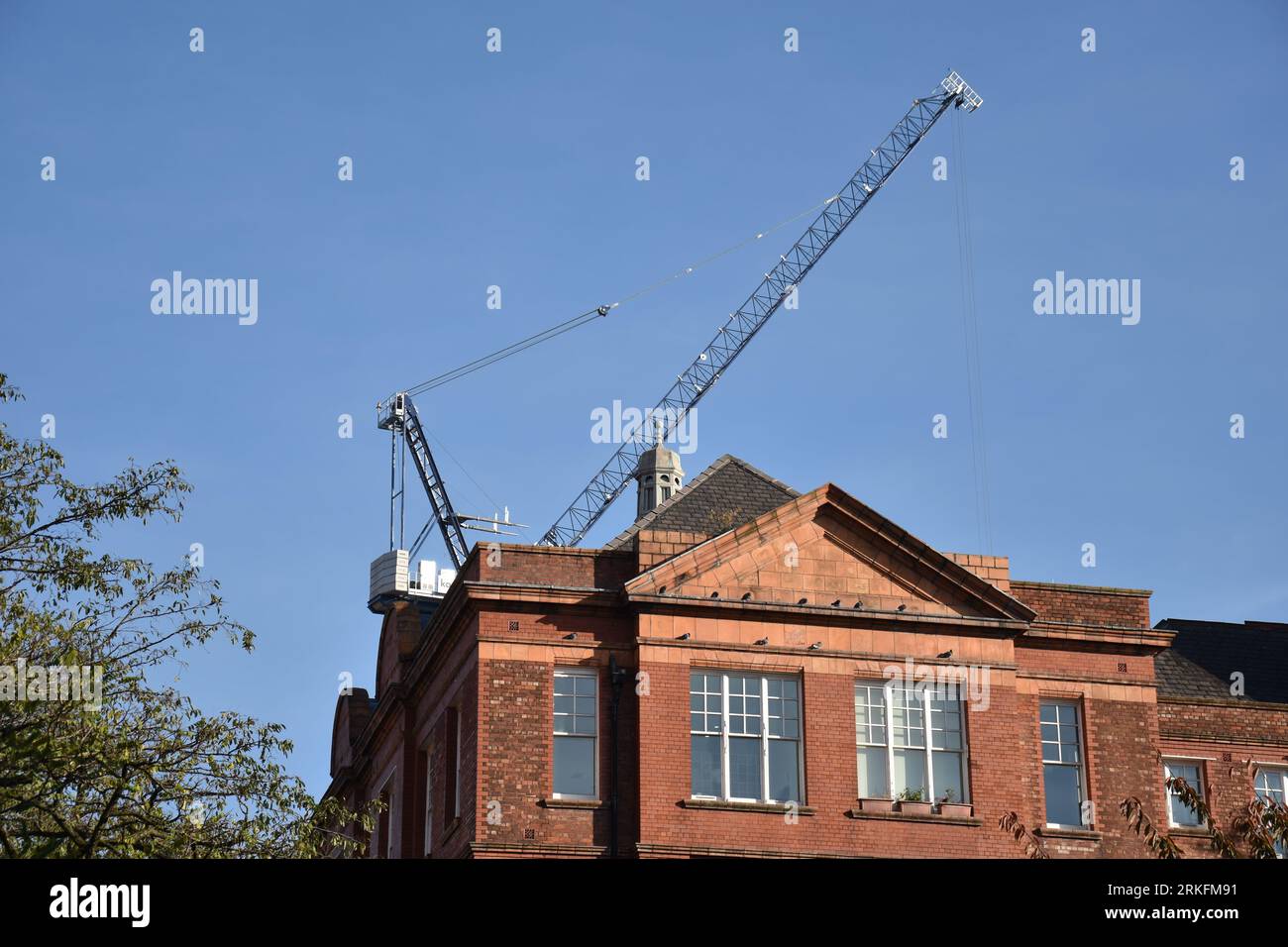 Une grue de construction sur le toit d'un vieux bâtiment traditionnel en briques rouges Banque D'Images