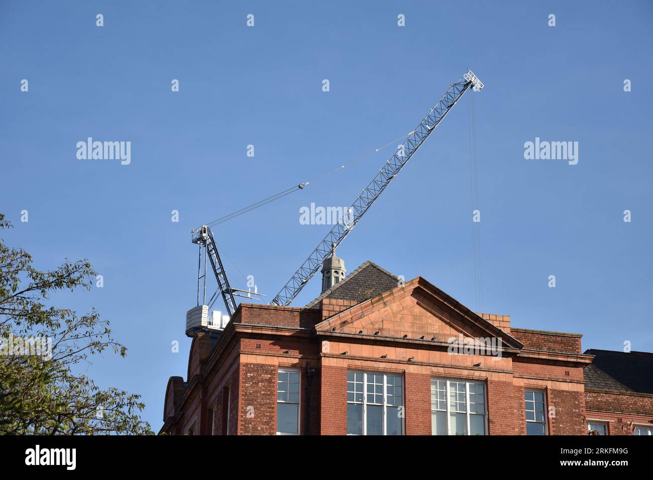 Une grue de construction sur le toit d'un vieux bâtiment traditionnel en briques rouges Banque D'Images