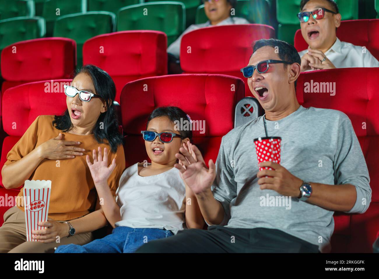 La famille asiatique heureuse de père, mère, fille et grand-mère chérit les moments de week-end au cinéma, partageant la joie et la convivialité tout en regardant un Banque D'Images