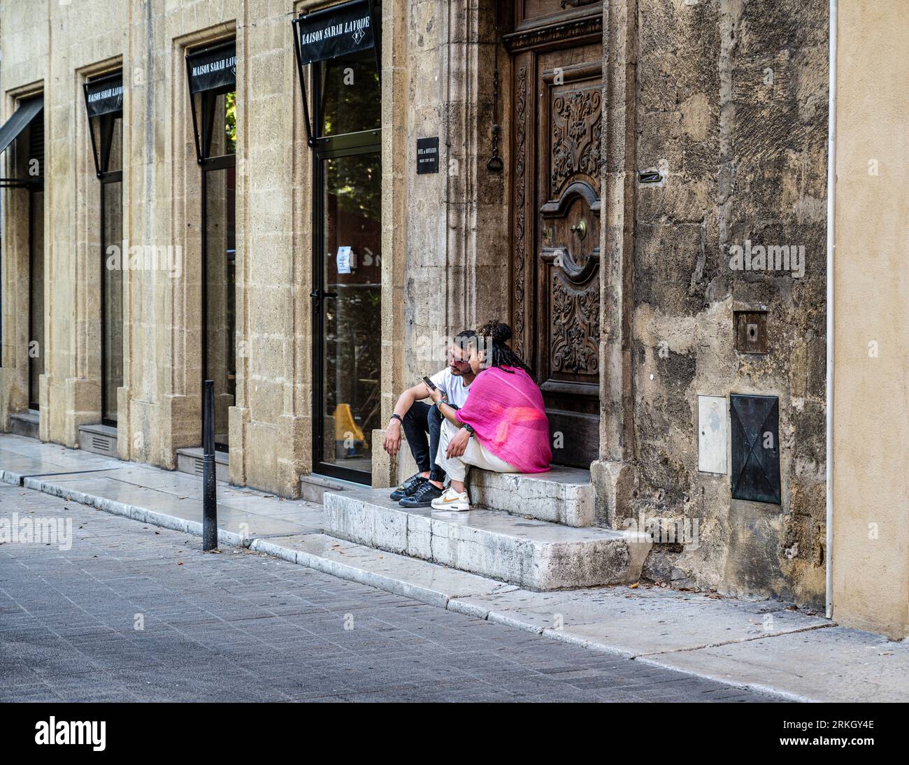 AIX-en-Provence, France -- 12 août 2023. Un couple est assis dans une porte regardant un téléphone portable sur un fay chaud. Banque D'Images