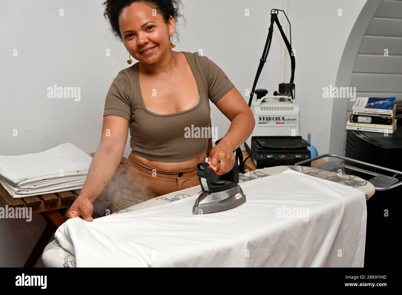 Jolie jeune femme travaillant dans les draps de repassage de l'hôtel avec fer à vapeur Banque D'Images