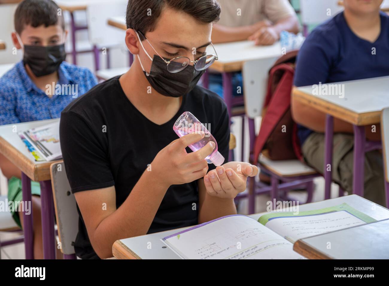 Adolescent à l'école stérilisant ses mains tout en portant un masque facial pour prévenir l'infection Banque D'Images