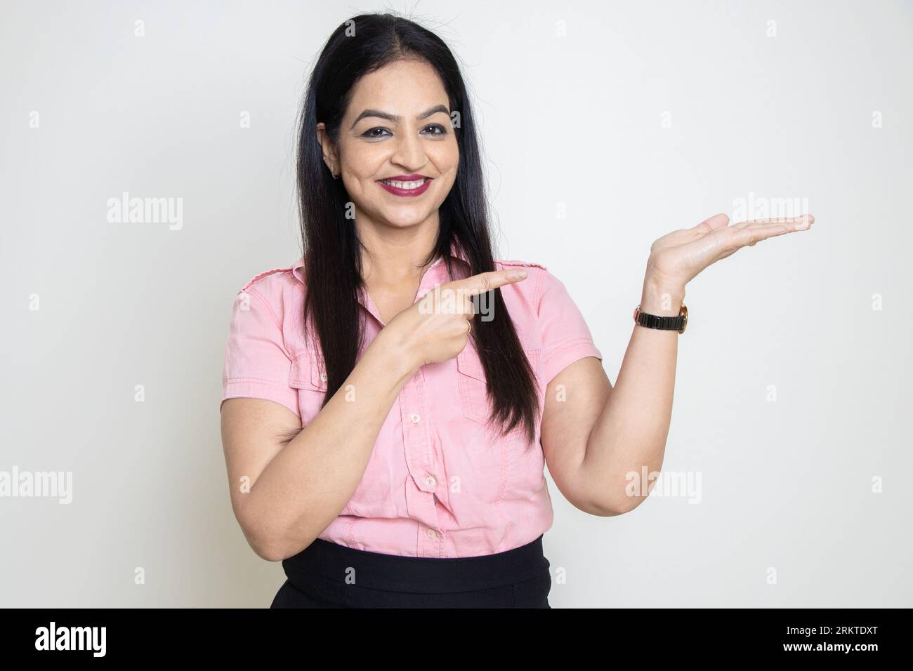 Femme indienne heureuse portant chemise rose formelle pointant vers les mains vides isolé sur fond blanc. Regardez ici, Publicité et promotion. Banque D'Images