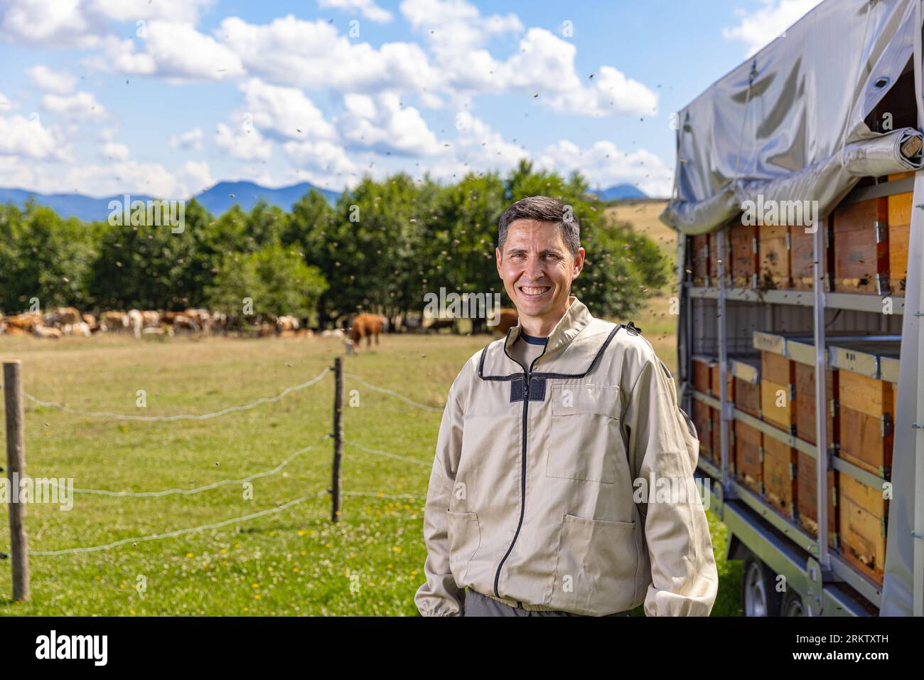 Portrait d'un apiculteur mâle heureux travaillant dans un rucher près des ruches avec des abeilles. Banque D'Images