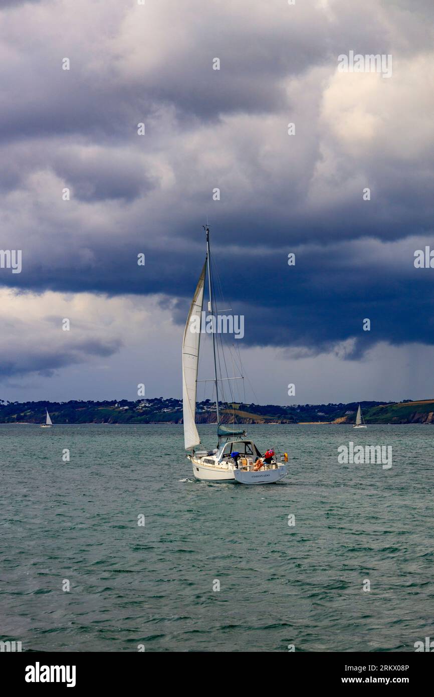 Un yacht fait son chemin vers le bas de la rivière FAL hors de Falmouth sous un ciel sombre, Cornwall, Angleterre, Royaume-Uni Banque D'Images