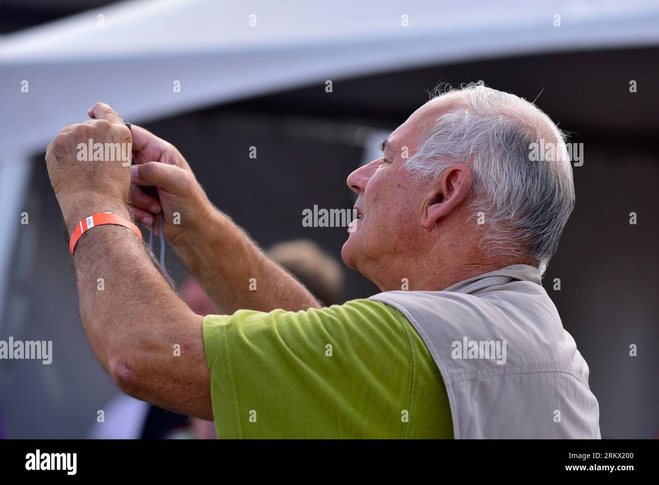 Un homme âgé regarde attentivement l'écran de son appareil photo, qui est en grande partie caché dans ses mains. Sur son poignet gauche, il porte une bande orange Banque D'Images