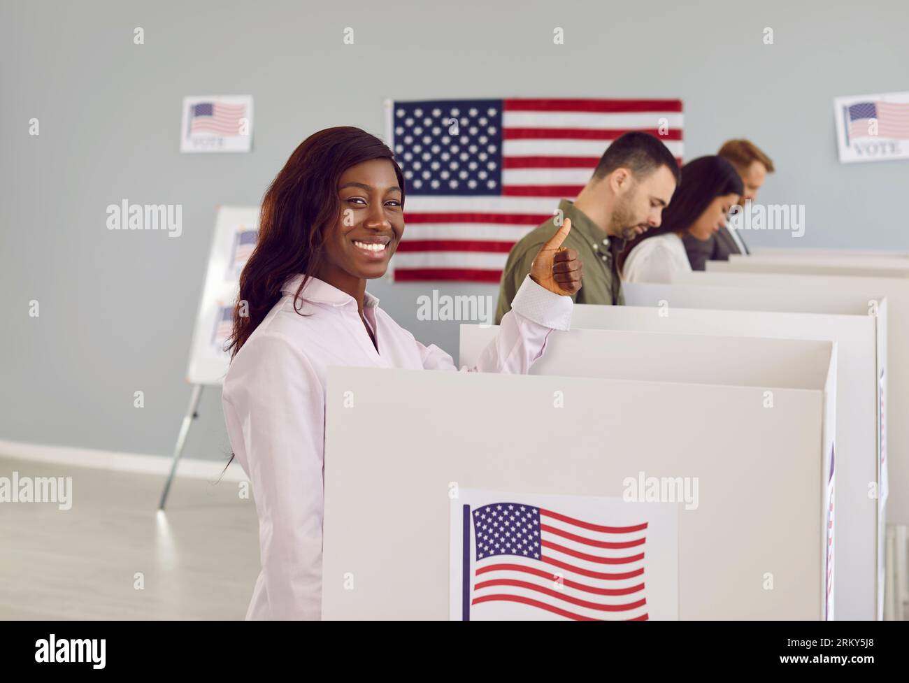 Heureuse femme votante américaine mettant son bulletin de vote dans la poubelle le jour de l'élection debout au centre de vote. Banque D'Images