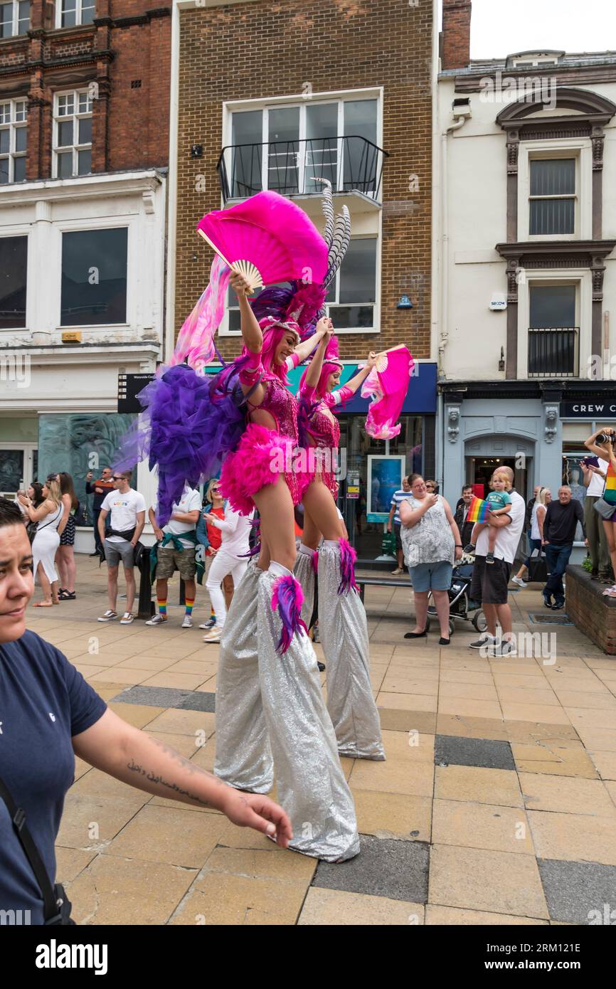 Deux jeunes femmes sur pilotis en costumes fantaisie agitant des fans de couleur dans Lincoln Pride Parade, High Street, Lincoln City, Lincolnshire, Angleterre, ROYAUME-UNI Banque D'Images