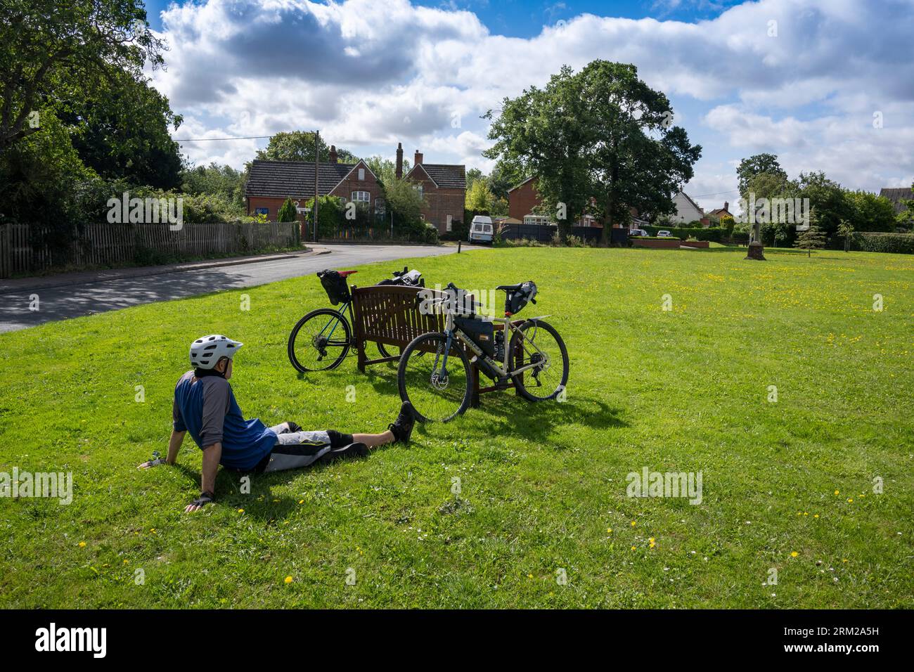 Un homme prend un repos d'une balade à vélo sur un vert de village dans la campagne du Norfolk Banque D'Images