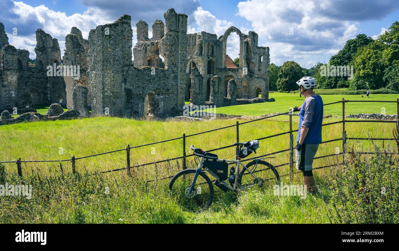 Un homme se tient près de son vélo de bikepacking profitant de la vue sur les ruines du Prieuré de Castle Acre à Castle Acre Norfolk Angleterre Royaume-Uni Banque D'Images