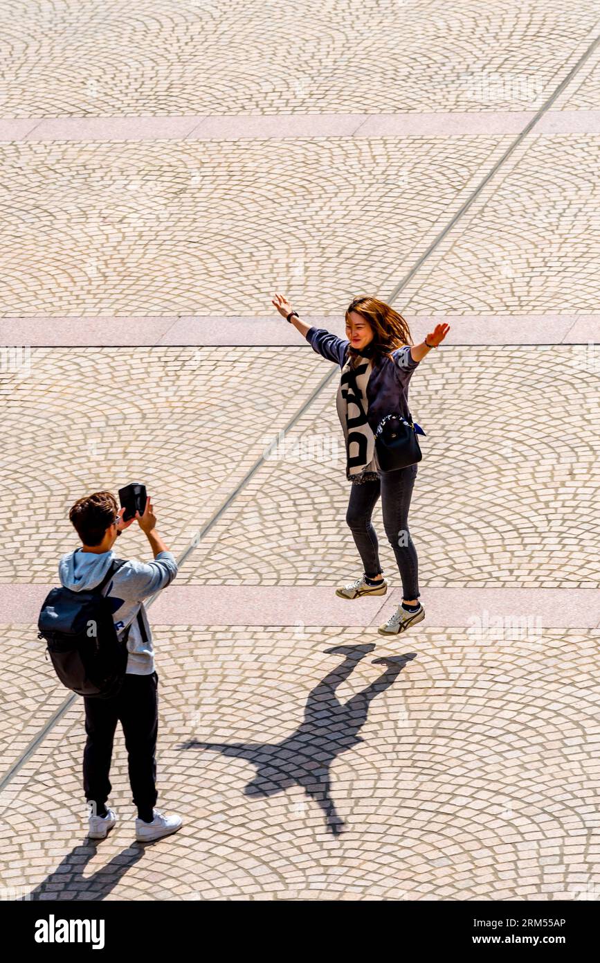 Un jeune homme utilise un téléphone portable pour photographier une jeune femme faisant un saut d'étoile sur le parvis de l'Opéra de Sydney en Australie Banque D'Images