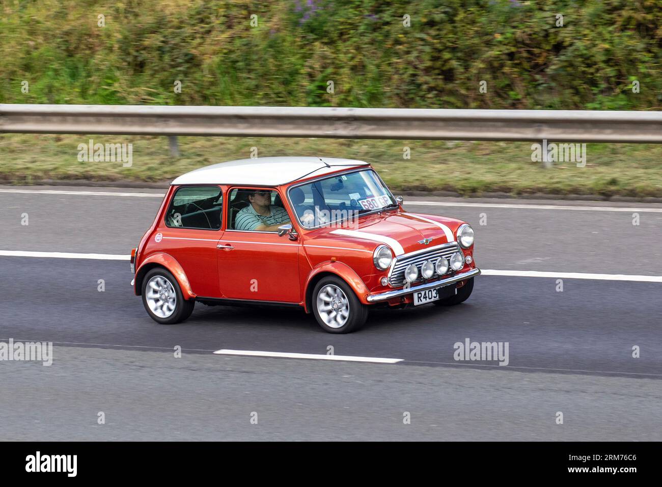 Années 1998 90 années 1990 British Orange Rover Mini Cooper travaille, rayures blanches de course ; voyageant à grande vitesse sur l'autoroute M6 dans le Grand Manchester, Royaume-Uni Banque D'Images