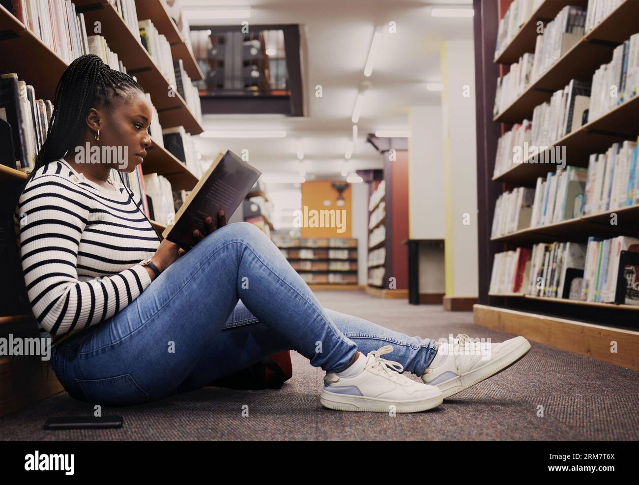 Recherche, livre et une femme noire dans une bibliothèque pour la lecture, les connaissances universitaires ou étudier sur le sol. Bourse, étudiante et une fille africaine à A. Banque D'Images