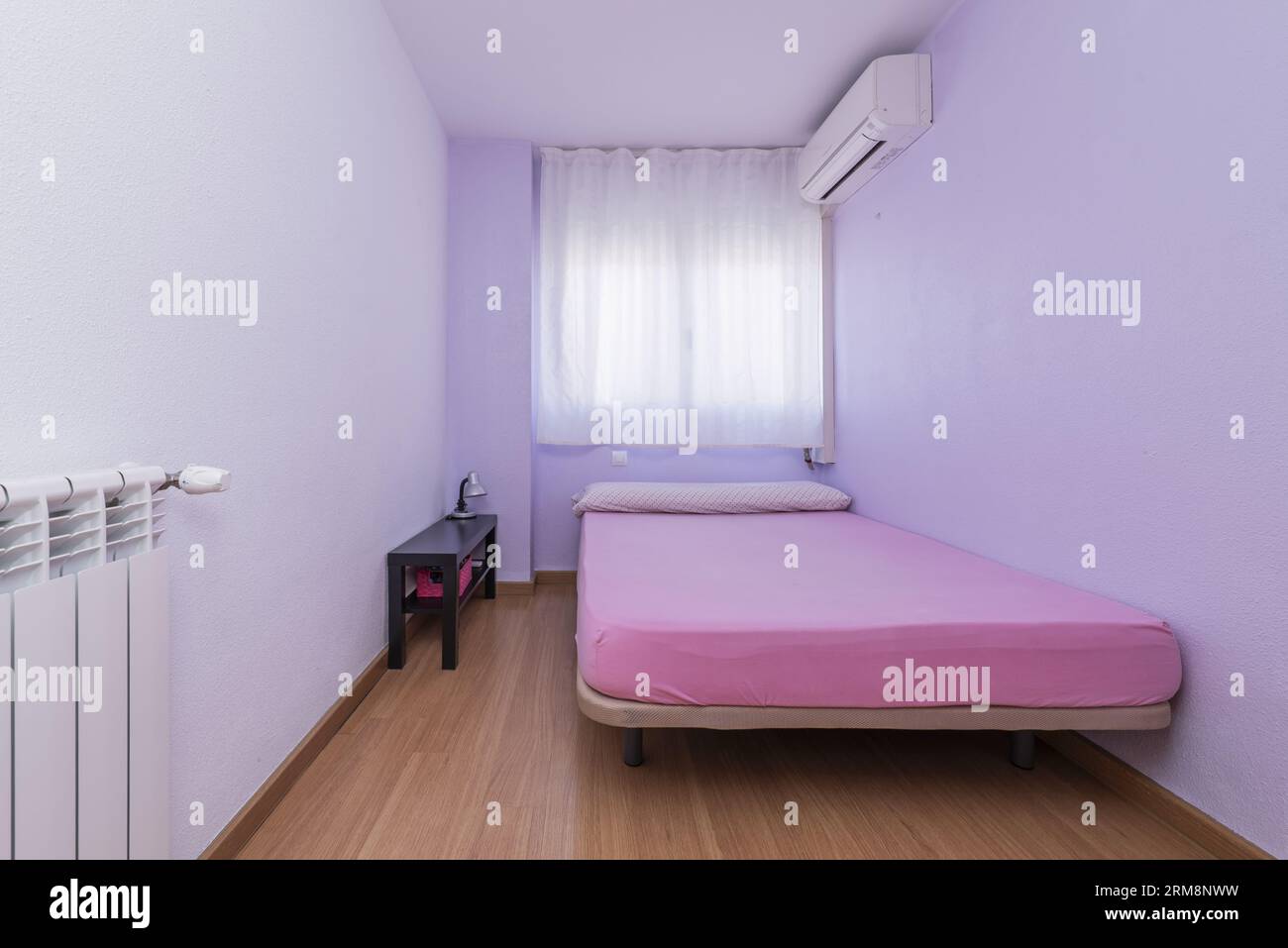 Chambre avec un lit simple sans vêtements, un climatiseur, une fenêtre avec rideaux, parquet et un radiateur en aluminium Banque D'Images