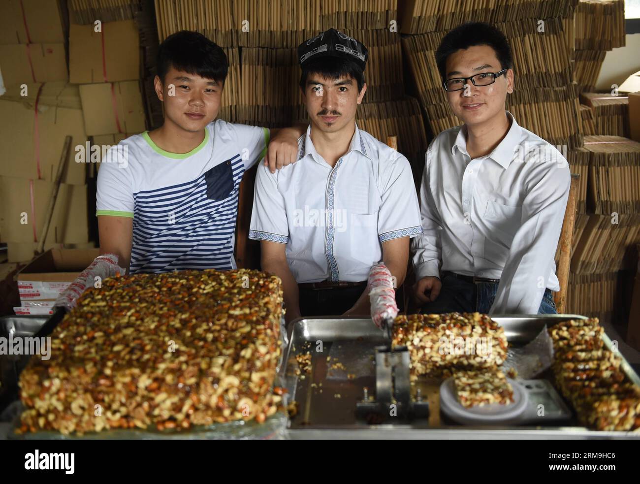 Adil Memettur (C) et ses partenaires commerciaux Jiang Jinya (R) et Jiang Chunyang posent pour des photos dans leur atelier de confection Matang à Changsha, capitale de la province du Hunan en Chine centrale, le 22 mai 2014. Adil Memettur est étudiant à l’Université des Sciences et technologies de Changsha. Avec deux de ses camarades de classe, Jiang Jinya et Jiang Chunyang, le jeune homme de 23 ans dirige maintenant une entreprise en ligne vendant le Matang, une confiserie ouïgoure originaire de la région autonome ouïgoure du Xinjiang du nord-ouest de la Chine. En décembre 2012, un villageois du Hunan s'est battu avec des vendeurs de rue ouïgour après des disputes sur le M Banque D'Images