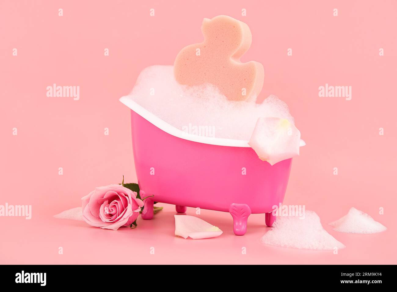 Petite baignoire avec mousse, fleur de rose et éponge sur fond rose Banque D'Images