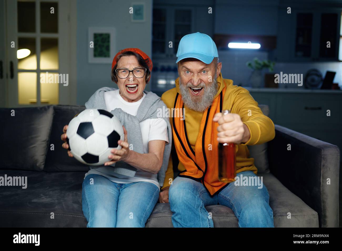 Joyeux couple de famille senior regardant un match de football à la télévision à la maison Banque D'Images