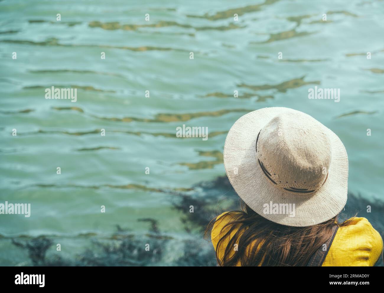 Vue arrière d'une élégante femme habillée portant un chapeau et assise au bord de l'eau à Venise. Banque D'Images