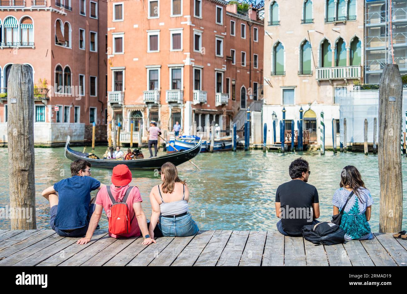 Venise, Italie - Mai 30 2023 : touristes assis sur un quai de bateau en bois et profitant de la scène idyllique sur le Grand Canal à Venise. Banque D'Images