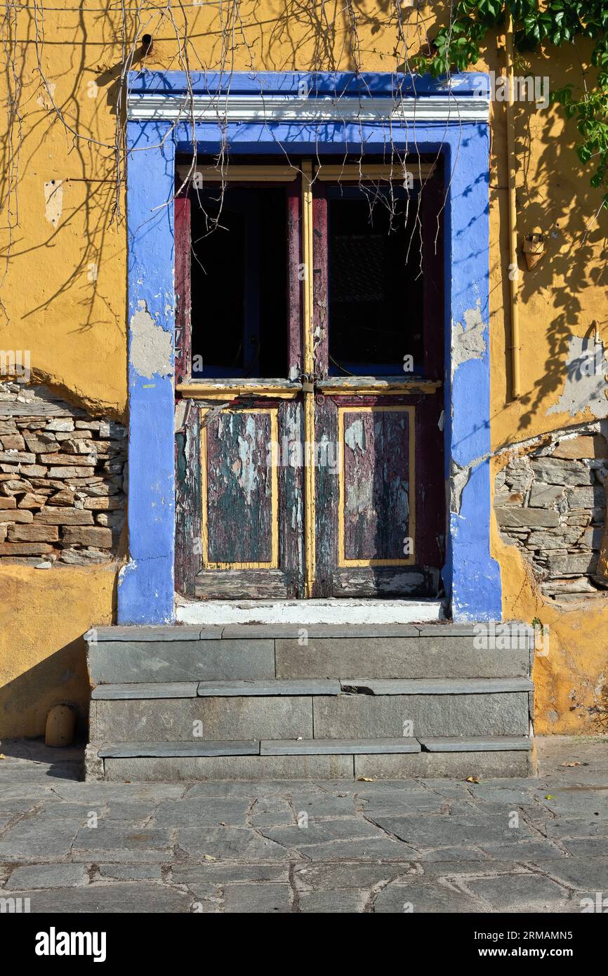Belle entrée avec vieille porte en bois, linteau bleu à violet, mur jaune et escalier en ciment pendant la lumière chaude de l'après-midi, dans la ville d'Eleftheroupoli Banque D'Images