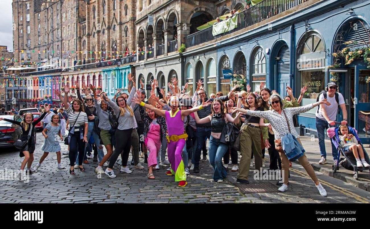 Grassmarket, Édimbourg, Écosse, Royaume-Uni. 27 août 2023. Silent Disco dirigé par David pour Guru Dudu visites à pied font leur chemin à travers Grassmarket et dans Victoria Street dans le centre-ville. Ces événements fréquents ont reçu des commentaires négatifs de certains habitants car les participants chantent souvent les chansons sur leurs écouteurs à haute voix, d'autres passants sont amusés par la scène. Crédit : Archwhite/alamy Live News. Banque D'Images