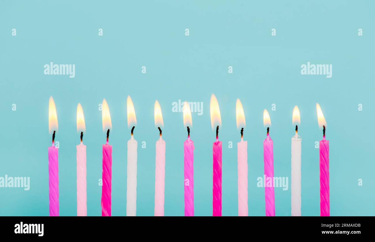 11 bougies d'anniversaire de couleur rose et blanche brûlant dans une rangée isolée sur bleu. Concept de carte de joyeux anniversaire. Bord inférieur de la bordure. Banque D'Images