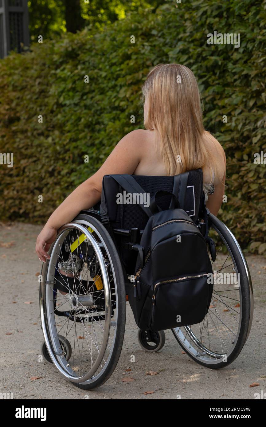 Jeune femme avec taille courte sur fauteuil roulant profite du temps à Green Park le jour de l'été. Vue arrière de la femme adulte handicapée pleine longueur. Solitude Banque D'Images