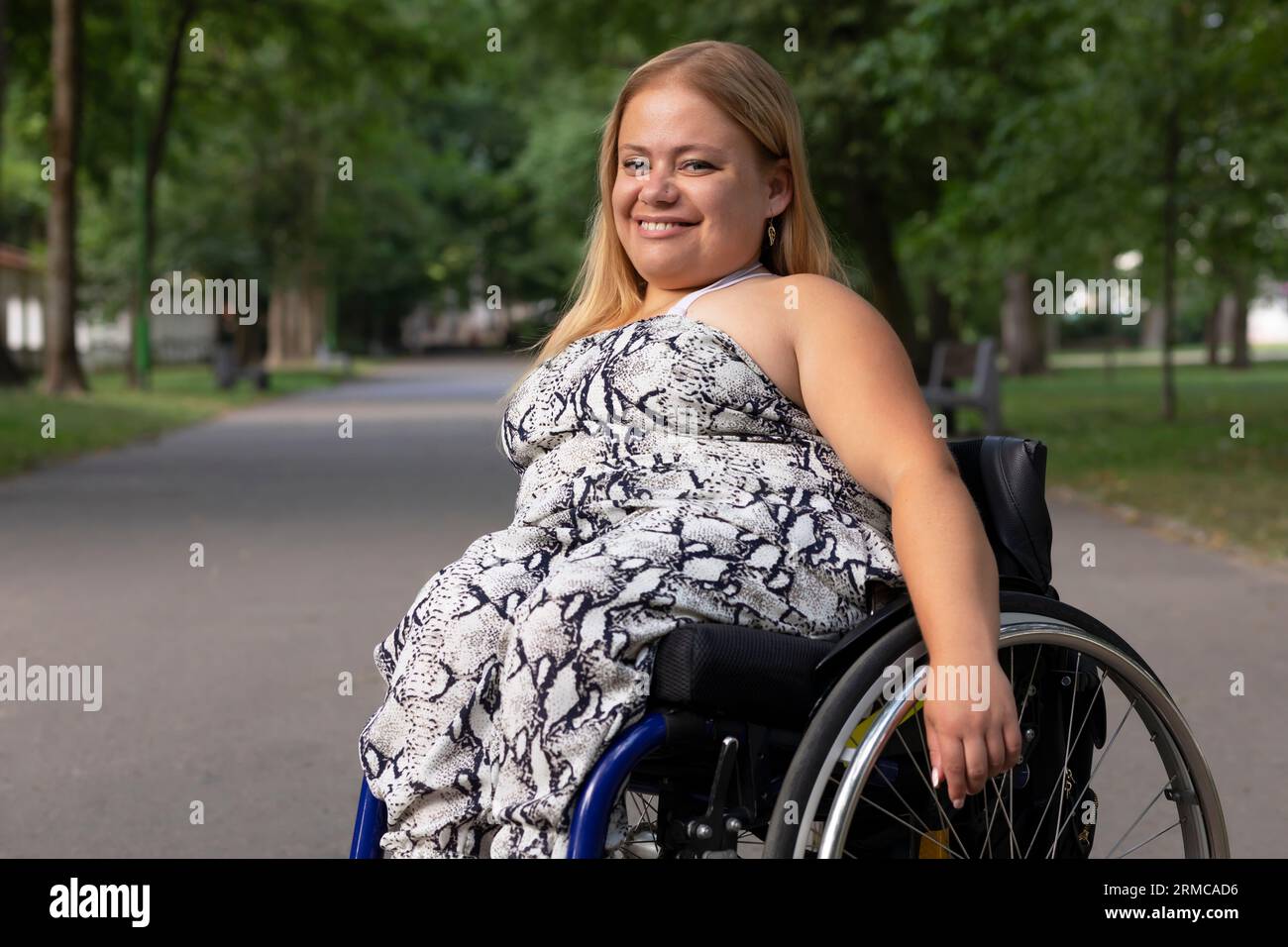 Souriant Happy Young Woman avec petite stature sur fauteuil roulant profite du temps dans Green Park au jour d'été. Femme adulte handicapée. Copier l'espace pour le texte Banque D'Images