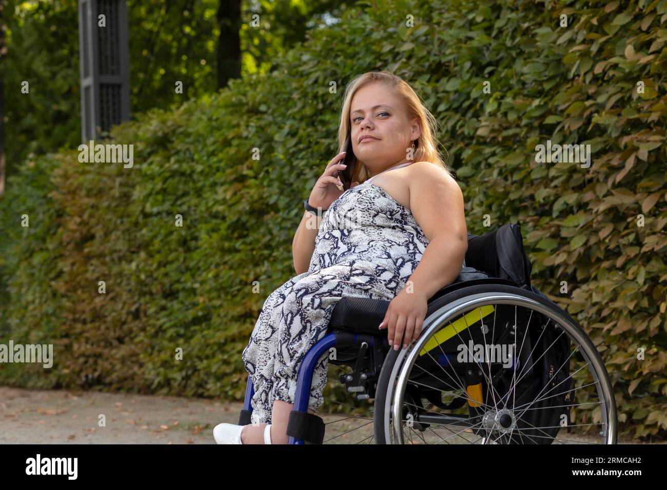 Souriant jeune femme de petite taille en fauteuil roulant parle sur smartphone à Green Park à Summer Day. Femme adulte handicapée. Copier l'espace pour Banque D'Images