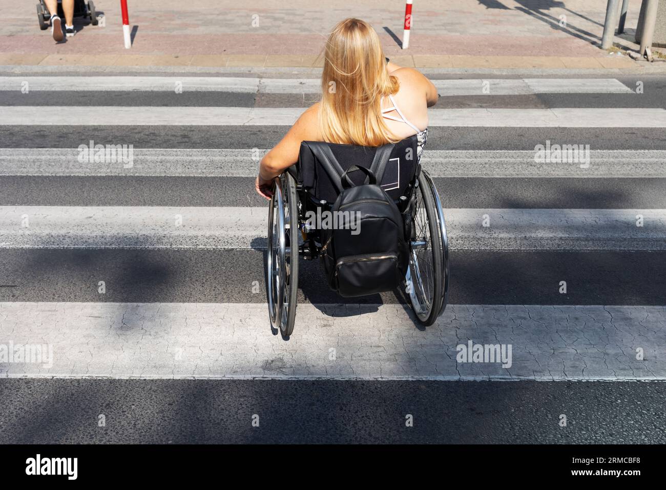Jeune fille de petite taille sur fauteuil roulant traversant la route, Crosswalk Street dans la ville le jour de l'été. Femme adulte avec handicap physique appréciant Banque D'Images