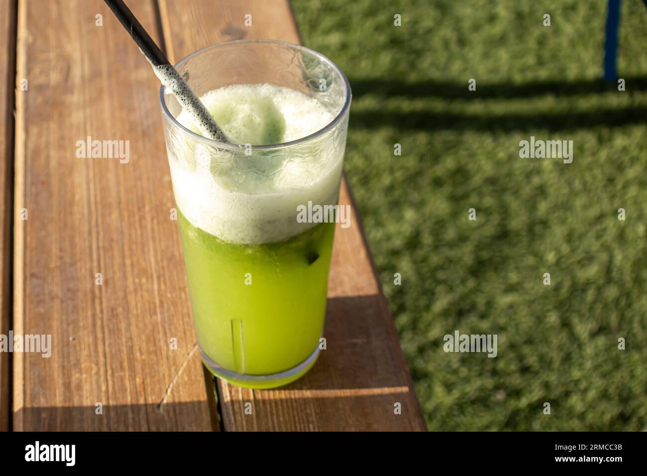 Boisson smoothie verte en verre avec de la paille sur une table en bois contre de l'herbe verte Banque D'Images