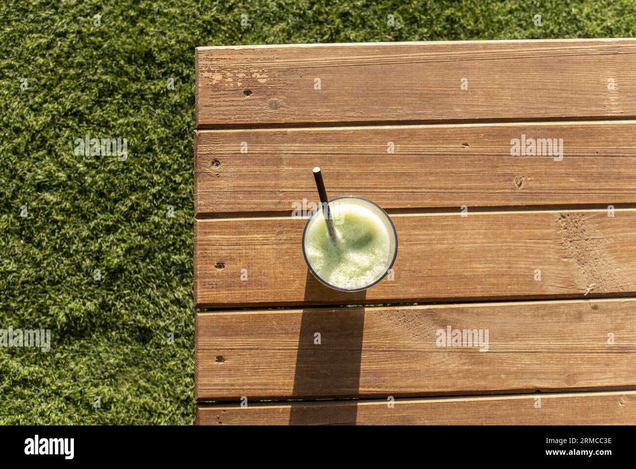 Boisson smoothie verte en verre avec de la paille sur une table en bois contre de l'herbe verte Banque D'Images