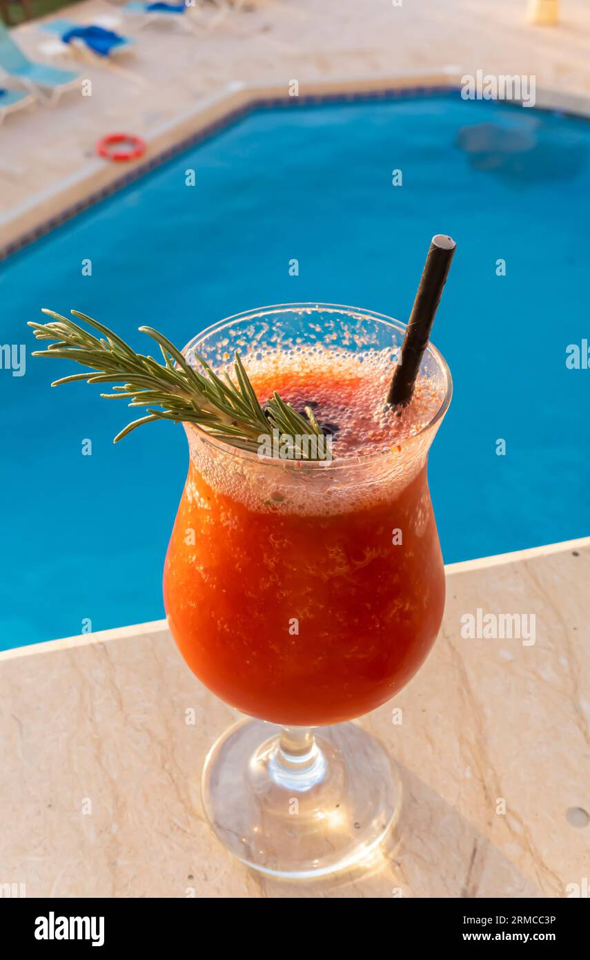 Verre de cocktail smoothie au jus de fraise avec paille contre une piscine lagon bleu Banque D'Images