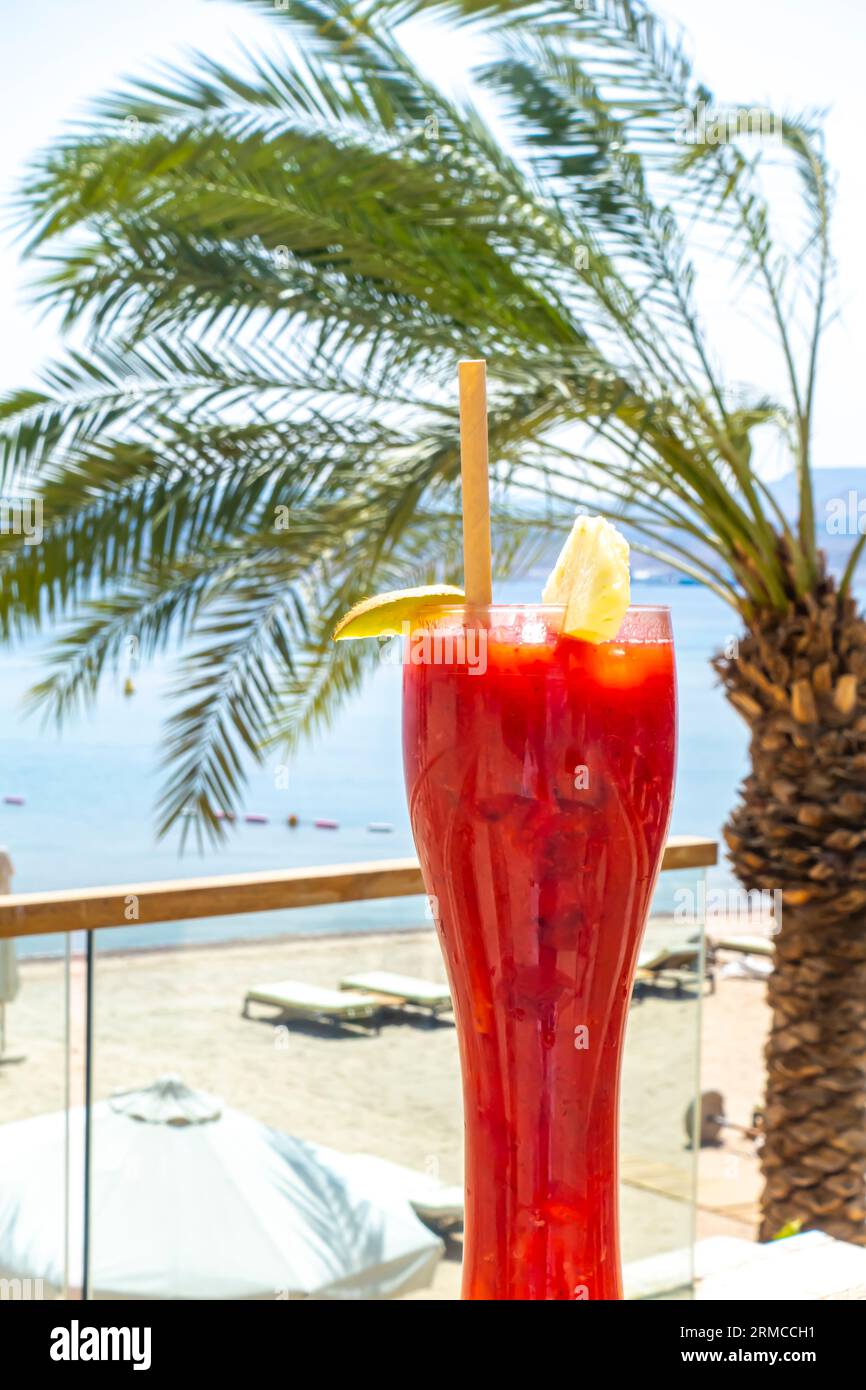 Verre de cocktail smoothie au jus de fraise au citron contre un paysage tropical, mer d'Arabie. Concept de boissons des stations de plages tropicales Banque D'Images