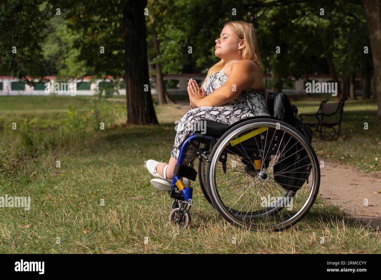Jeune femme avec la taille courte sur fauteuil roulant médite, se relaxant dans Green Park le jour d'été. Pleine longueur Femme adulte handicapé aime le temps Banque D'Images