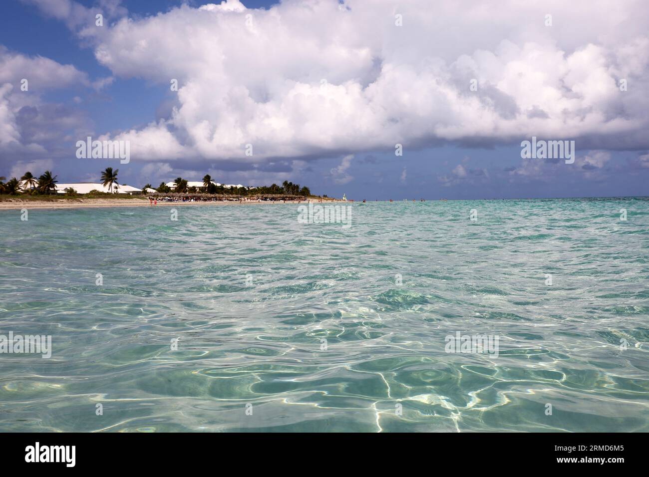 Vue défocalisée de la surface de l'océan à la plage tropicale avec les gens, la côte sablonneuse et les cocotiers. Station balnéaire sur l'île des Caraïbes avec de l'eau claire Banque D'Images