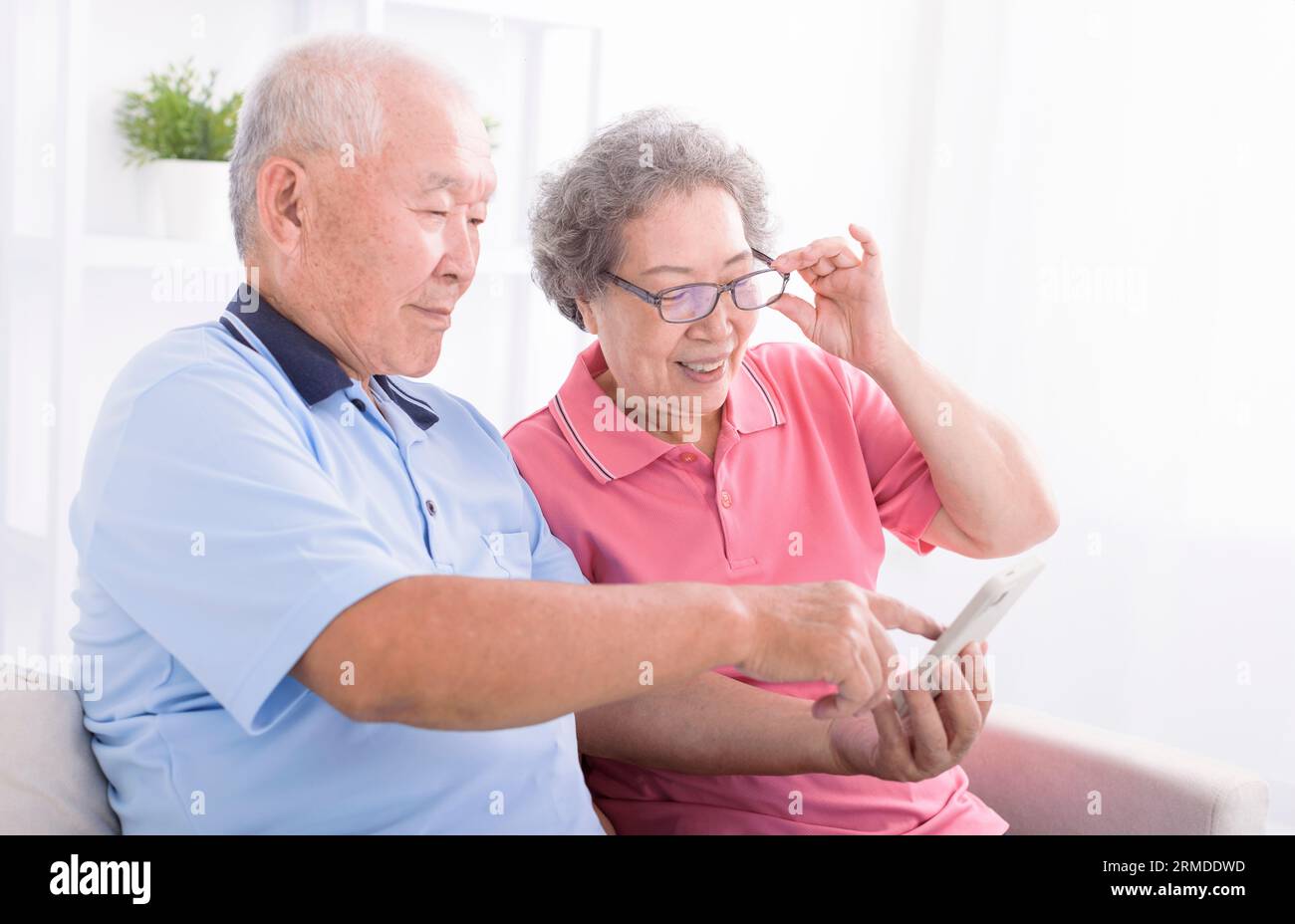 Heureux couple senior utilisant le téléphone cellulaire ensemble à la maison, surfer sur Internet, assis sur le canapé Banque D'Images