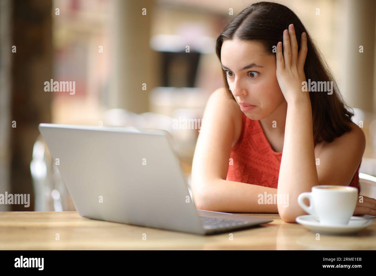 Femme perplexe vérifiant le contenu absurde de l'ordinateur portable dans une terrasse de bar Banque D'Images