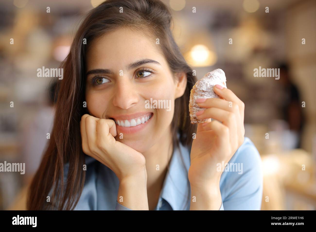 Femme heureuse avec sourire de beauté tenant croissant dans un intérieur de bar Banque D'Images