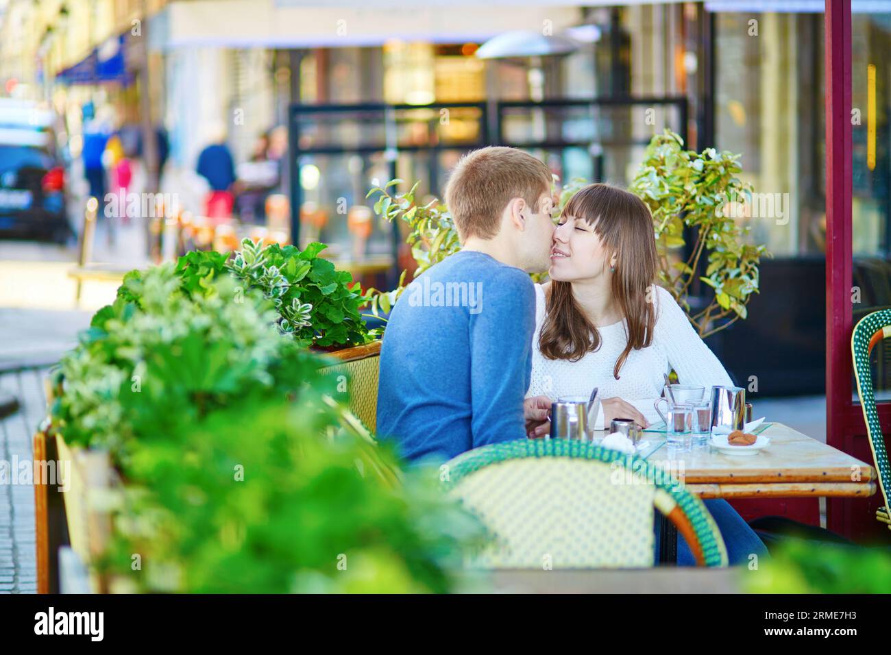 Couple dans un café de rue parisien, boire du chocolat chaud et s'embrasser Banque D'Images